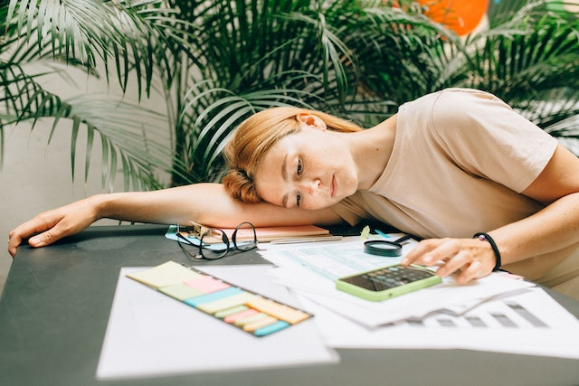 Overwhelmed woman calculating invoices at a desk, struggling with manual billing and paperwork in need of automation.