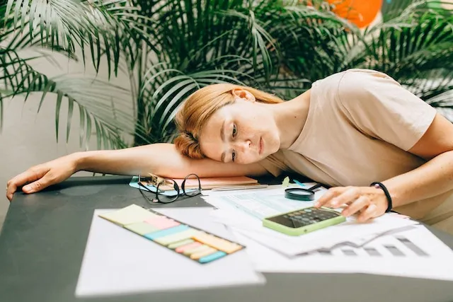 Overwhelmed woman calculating invoices at a desk, struggling with manual billing and paperwork in need of automation.