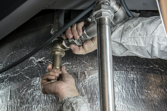 Plumber repairing pipes under a sink, professional plumbing services for leak repairs and maintenance.