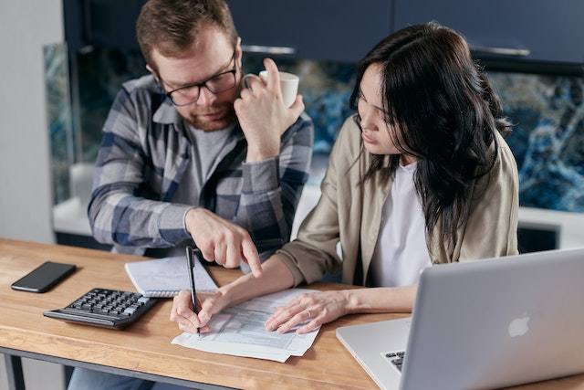 Two professionals reviewing a proforma invoice at a desk with a laptop, calculator, and documents, understanding the purpose and use of proforma invoices in business transactions.